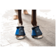 Die Vorderbeine eines Pferdes tragen blaue Hufschuhe mit schwarzen Riemen und Fellfutter, stehen auf einer Kopfsteinpflasteroberfläche.