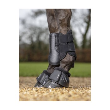 Eine Nahaufnahme der Beine eines Pferdes, das schwarze Schutzstiefel und Wickel trägt, vor einem verschwommenen Außenhintergrund.