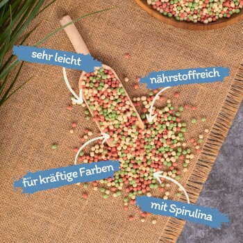 Bunte Haustierfutterpellets um eine Holzschaufel, mit deutschen Etiketten: "sehr leicht", "nährstoffreich", "lebendige Farben", "mit Spirulina."