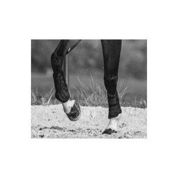 Eine Nahaufnahme in Schwarz-Weiß von den Beinen eines Pferdes in Bewegung, das Schutzstiefel an den Vorderbeinen trägt, mit sandigem Boden darunter.