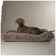 Ein grauer Weimaraner-Hund liegt auf einem plüschigen, rechteckigen Hundebett mit gestepptem Design und schaut neugierig in die Kamera.