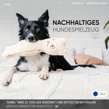 Ein schwarz-weißer Hund hält ein Plüschknochen-Spielzeug, mit Text darüber, dass es aus recycelten Materialien hergestellt ist.