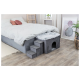 Ein gemütliches Haustierhaus mit Treppen, neben einem Bett mit einer grauen Bettdecke und Kissen, in einem hellen, modernen Schlafzimmer.