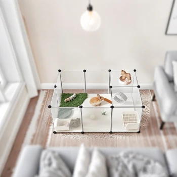 Ein transparenter Tierkäfig mit einem Kaninchen, das an einer Karotte knabbert, einer kleinen Katzenfigur und verschiedenen Spielzeugen auf Gras und Bettzeug.