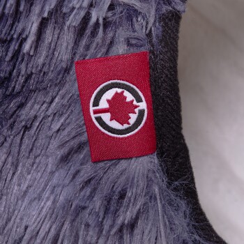 Nahaufnahme eines plüschigen Haustierbettes mit einem roten Etikett mit einem schwarzen Kreis und einem weißen Ahornblatt-Logo, vor einem weichen grauen Fell.