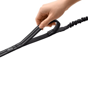 Hand hält schwarze Bungee-Hundeleine mit gepolstertem Griff, reflektierend gepunkteter Naht und 'HUNTER'-Anhänger.