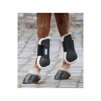 Eine Nahaufnahme von Pferdebeinen, die schwarze Schutzstiefel mit weißem Fleecefutter tragen, stehen auf einem Kopfsteinpflasterweg.