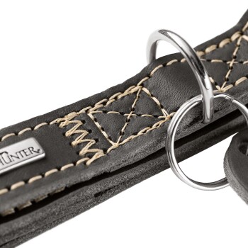 Nahaufnahme eines schwarzen Lederhundehalsbands mit hellbrauner Naht, Metall-D-Ringen und Markenanhänger „HUNTER“