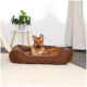 Ein brauner Hund ruht sich bequem in einem plüschigen Hundebett auf einem weichen Teppich aus, mit einer grünen Topfpflanze auf einem weißen Tisch im Hintergrund.