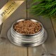 Eine Edelstahlschüssel für Haustierfutter, gefüllt mit hochwertigem Nassfutter für Katzen, mit einer strukturierten, fleischigen Mischung, mit einer grünen Pflanze im Hintergrund.