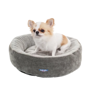 Ein kleiner Hund sitzt in einem runden, plüschigen grauen Haustierbett mit weißem Innenraum, das ein blaues Logo mit der Aufschrift "WALLACE & JONES" zeigt.