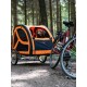 Ein Haustieranhänger in Orange und Schwarz, entworfen für das Radfahren, geparkt auf einem Waldweg neben einem Fahrrad.