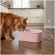 Rotgetigerte langhaarige Katze trinkt aus einem rosa elektrischen Trinkbrunnen auf einem Holzfußboden in einer hellen Küche.