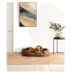 Ein brauner Hund, der in einem gemütlichen Haustierbett auf einem Holzboden ruht, mit einem modernen abstrakten Gemälde an der Wand und einem kleinen Tisch mit Pflanzen in der Nähe.