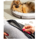 Ein flauschiger Pomeranian entspannt sich auf einem runden Haustierbett mit grauem Äußeren und weißem Inneren, während eine Hand den waschbaren Bezug aufzippt.