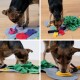 Ein kleiner Hund interagiert mit einer bunten Filzpuzzle-Matte und sucht nach versteckten Leckereien zwischen verschiedenen Stoffformen in Rot, Lila und Grün.