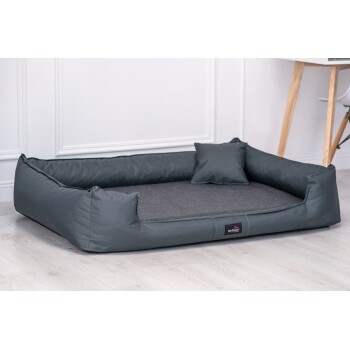 Ein gemütliches dunkelgraues Haustierbett mit erhöhten Rändern und einem kleinen passenden Kissen, vor einem hellen Holzboden und einer weißen Wand.