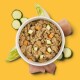 Schüssel mit Haustierfutter, die gehacktes Fleisch mit grünen Erbsen und gewürfelten Karotten zeigt, umgeben von frischen Spinatblättern und rohen Fleischstücken.