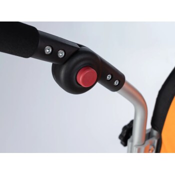 Nahaufnahme eines Haustierwagen-Griffs, mit einem schwarzen Griff und einem auffälligen roten Knopf, mit einem silbernen Rahmen und orangefarbenem Stoff.