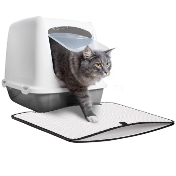 Eine graue Katze mit gelben Augen kommt aus einer weißen und grauen Katzentoilette, mit einer strukturierten weißen Matte davor.