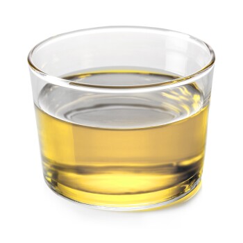 Ein klares Glas mit einer goldgelben Flüssigkeit, möglicherweise ein Ergänzungsfuttermittel oder Öl, vor einem weißen Hintergrund.