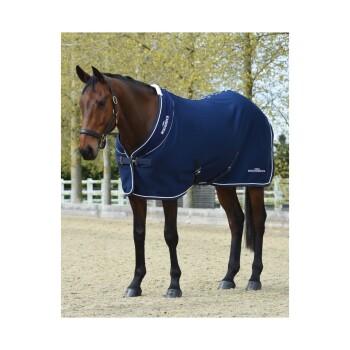 Ein braunes Pferd, das eine marineblaue Weatherbeeta-Decke trägt, steht in einer Außenarena mit Bäumen im Hintergrund.