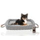 Ein kleiner schwarz-brauner Chihuahua liegt bequem auf einem weichen, grauen gewebten Haustierbett mit Griffen, begleitet von einem beigen Spielzeug.
