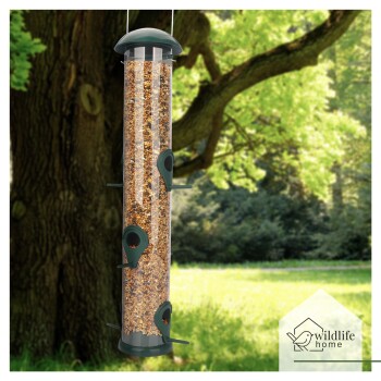 Ein hoher, transparenter Vogelhäuschen, gefüllt mit Samen, mit mehreren Futteröffnungen, die von einem Baum in einem üppigen grünen Park hängen.