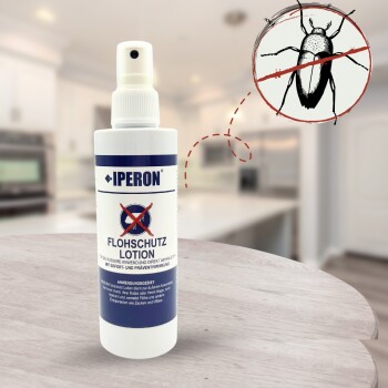 Weiße Sprühflasche mit der Aufschrift IPERON FLOHSCHUTZ LOTION und durchgestrichenem Flöhen-Symbol vor unscharfem Küchenhintergrund.