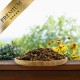 Holzschale mit getrockneten Grillen auf einer Holzbank, gelbe Blumen im Hintergrund, goldenes Band mit der Aufschrift „PREMIUM“