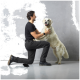 Ein Mann in einem schwarzen Hemd und einer Hose kniet und interagiert freudig mit einem Golden Retriever, der auf seinen Hinterbeinen steht, beide wirken glücklich.