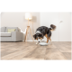 Schwarz-brauner Hund interagiert mit einem weißen automatischen Futterspender auf einem Holzboden in einem Wohnzimmer.