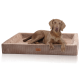 Ein brauner Hund liegt auf einem plüschigen, rechteckigen Haustierbett mit gerippter Textur und einem Lederetikett, vor einem weißen Hintergrund.