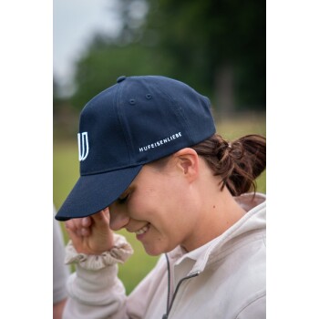 Eine Person trägt eine marineblaue Kappe mit dem Text "Hufeisenliebe" an der Seite und hält ihre Hand in der Nähe ihres Gesichts im Freien.