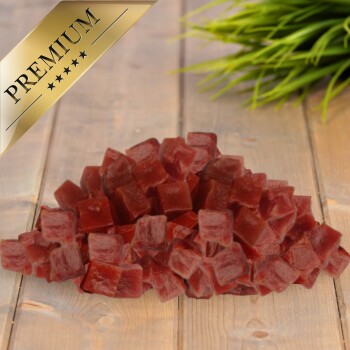 Haustierleckerlis in Premiumqualität in kleinen, würfelförmigen Stücken, die auf einer Holzoberfläche mit grünem Gras im Hintergrund präsentiert werden.