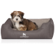Ein kleiner, flauschiger Hund sitzt bequem in einem grauen Haustierbett mit Rippendesign, mit dem Markennamen "KNUFFELWUFF" deutlich angezeigt.