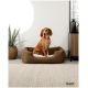 Ein braunes Hundebett mit einem weißen Kissen, in dem ein brauner Hund sitzt, umgeben von einer Pflanze und einem modernen Schrank.