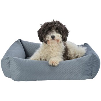 Ein flauschiger schwarz-weißer Hund, der in einem weichen, grauen Haustierbett mit gestepptem Muster entspannt.