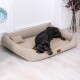 Ein schwarzer Dobermann liegt bequem auf einem beigen Hundebett mit einem kleinen Kissen, in einem hellen Raum mit hellen Holzböden.