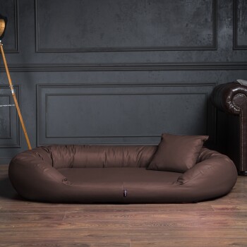 Braunes Lederhaustierbett mit passendem Kissen auf Holzboden vor einer dunkelgrauen vertäfelten Wand.