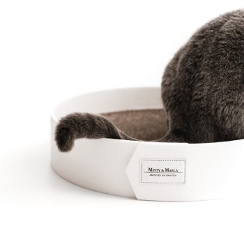 Ein grauer Katzenschwanz schaut aus einem runden, weißen Haustierbett mit der Aufschrift "MINTY & MARLA" heraus, mit dem Text "Also für dich und deine Katze."