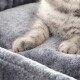 Nahaufnahme der Pfoten einer grauen Katze, die auf einem weichen, plüschigen grauen Haustierbett ruhen.