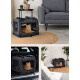 Orange getigerte Katze ruht in einem dunkelgrauen, weichwandigen Haustierträger auf einem gewebten Teppich neben einem grauen Sofa.