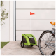 Ein grüner Haustieranhänger, der an einem Fahrrad befestigt ist, mit einer kleinen roten Fahne, geparkt auf einem Steinweg neben einer Wand und Gras.