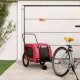 Ein pinkfarbener Haustieranhänger mit einem schwarzen Netzfenster und einer kleinen orangefarbenen Fahne, geparkt neben einem grauen Fahrrad auf einem Steinweg.