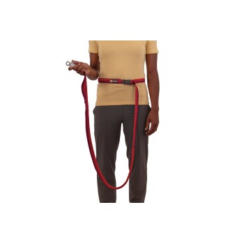 Eine Person, die ein gelbes Shirt und graue Hosen trägt, hält eine rote Hundeleine, die an einem Gürtel befestigt ist, bereit für einen Spaziergang.