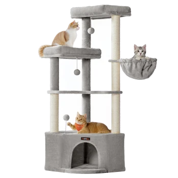 Drei Katzen auf einem mehrstufigen grauen Kratzbaum mit hängenden Bällen und einer Hängematte, eine Katze trägt ein oranges Halstuch.