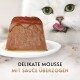Weiße Katze leckt sich die Lippen neben einer mit Sauce überzogenen Katzenmousse auf einem Teller; Text 'DELIKATE MOUSSE MIT SAUCE ÜBERZOGEN'