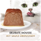Weiße Katze leckt sich die Lippen neben einer mit Sauce überzogenen Katzenmousse auf einem Teller; Text 'DELIKATE MOUSSE MIT SAUCE ÜBERZOGEN'