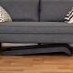 Ein modernes graues Sofa mit zwei dekorativen Kissen, eines mit einem schwarz-weißen Zickzackmuster, steht auf einem Holzboden.